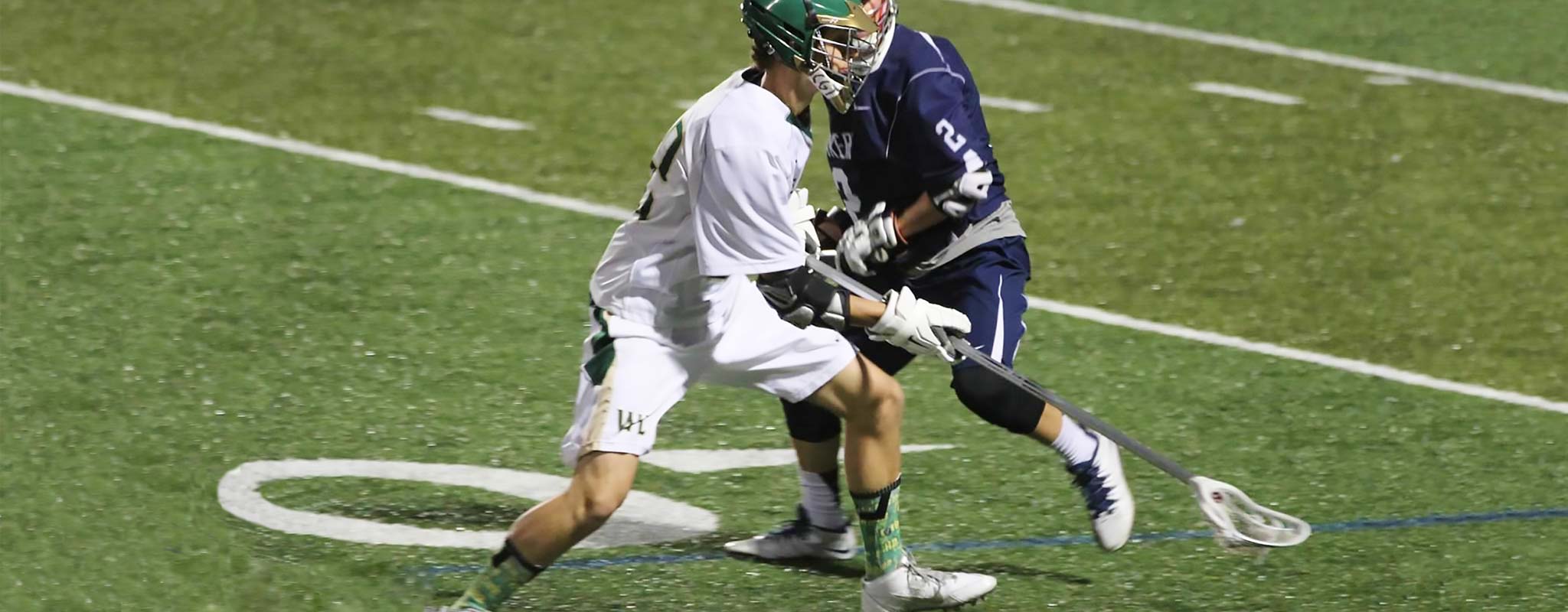 Two lacrosse players face off on the field.